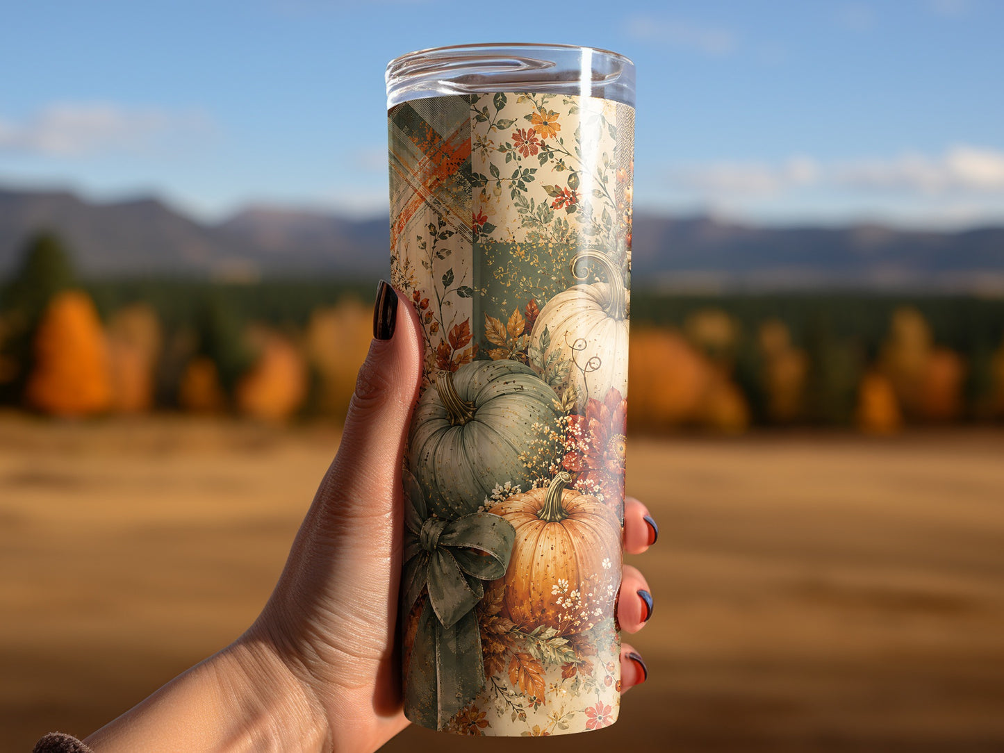 Tumbler with autumn floral and pumpkin pattern held by hand with blurred background.