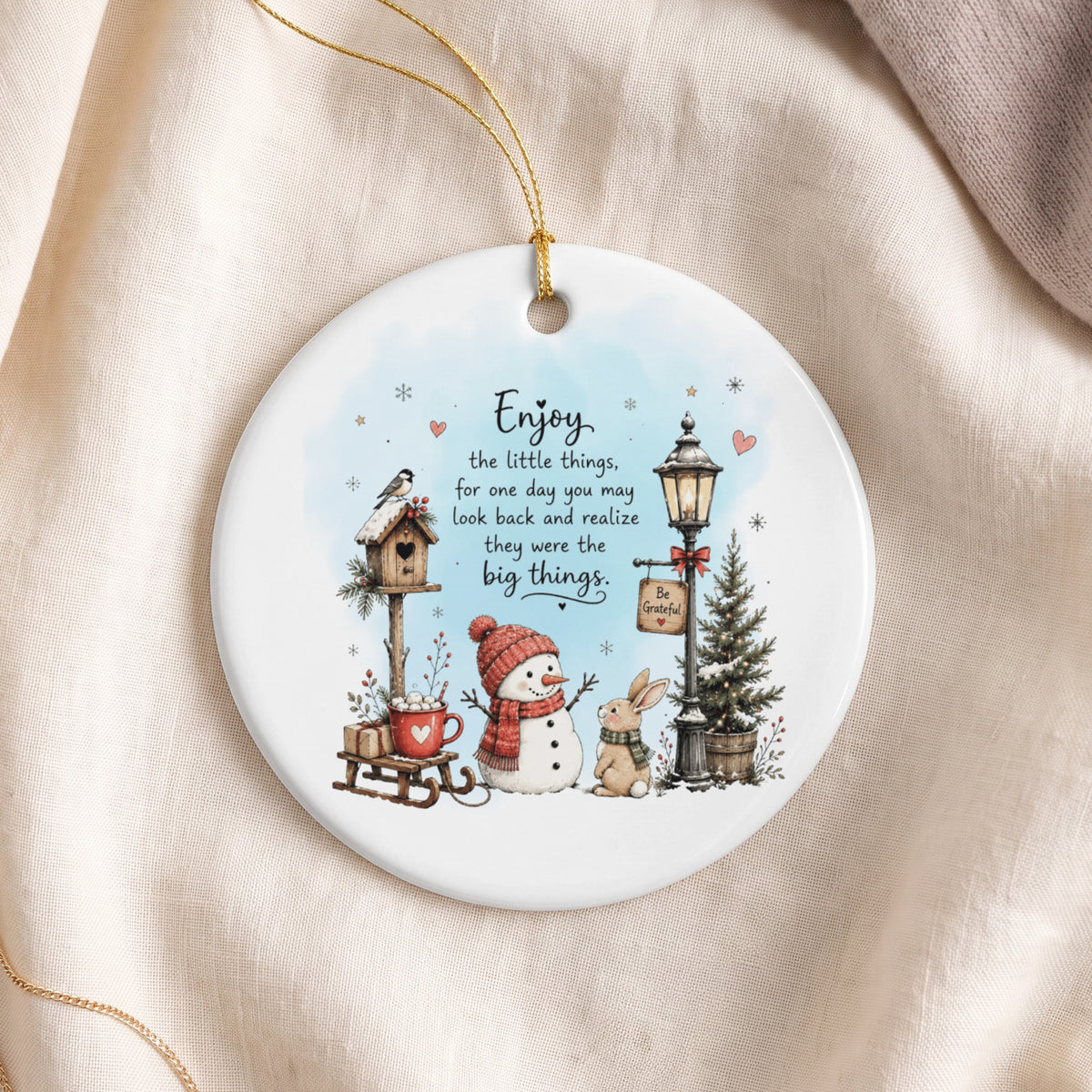 Round white ceramic ornament featuring a winter scene with a snowman, bunny, birdhouse, and inspirational text.