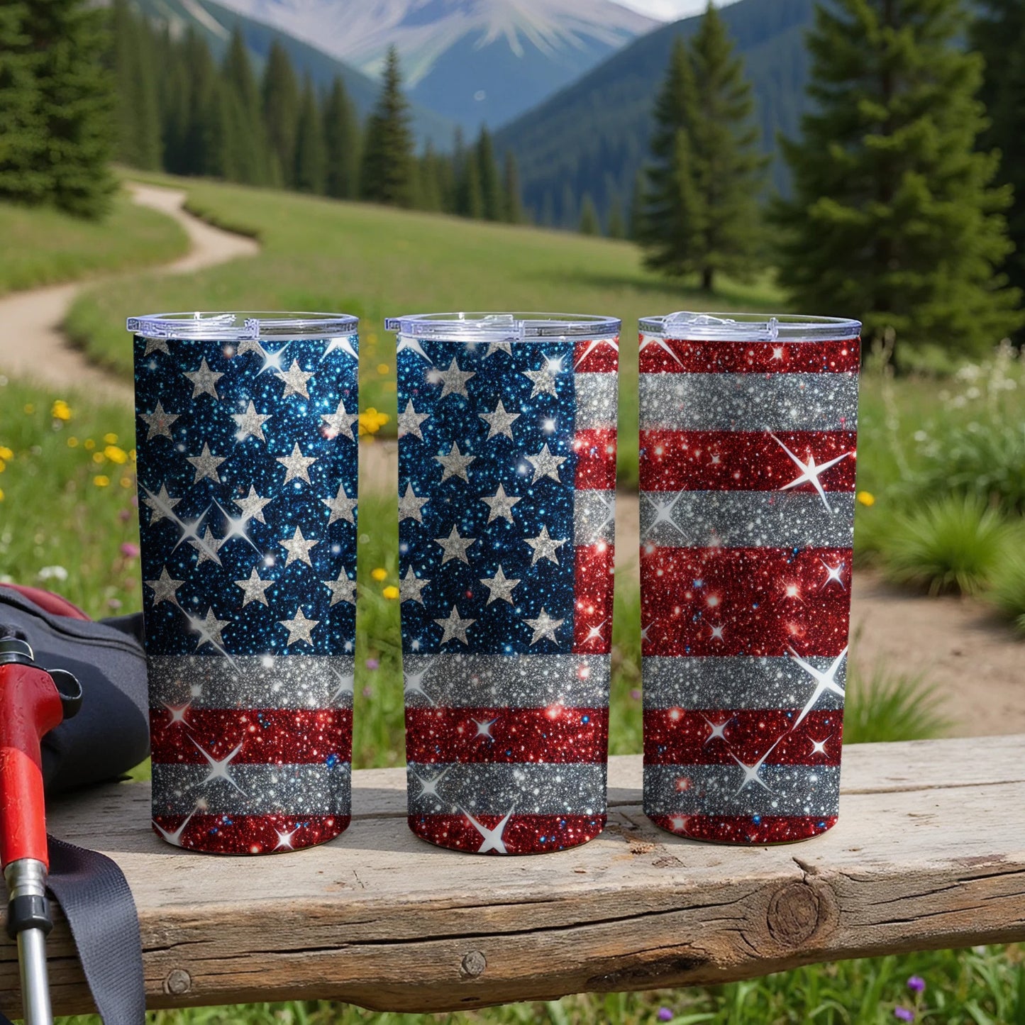 Three glittery American flag tumblers sit on a wooden surface outdoors.