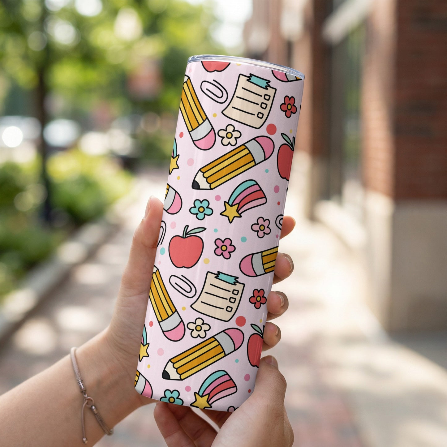 Pink tumbler with a pattern of pencils, apples, stars, and flowers.