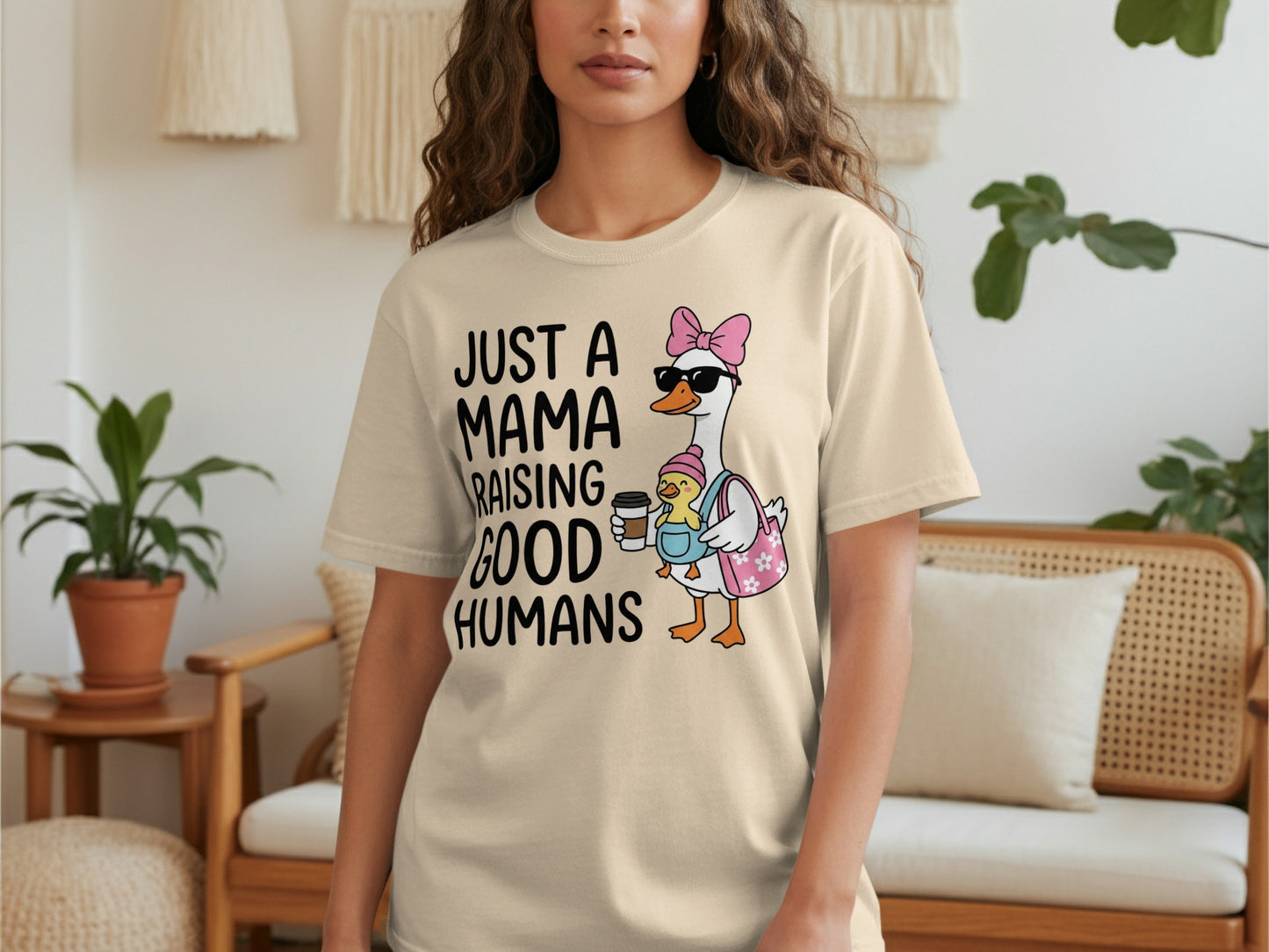 Cream t-shirt with a goose in sunglasses holding a baby and text "JUST A MAMA RAISING GOOD HUMANS".