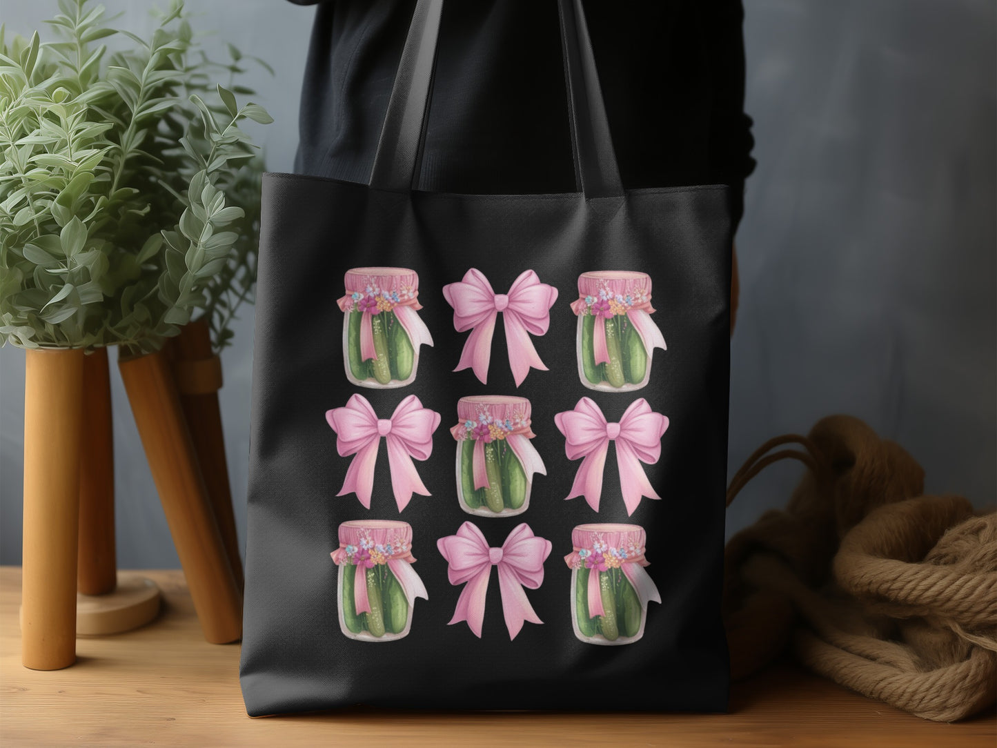 Nine jars of pickles with pink bows arranged in a 3x3 grid on a black tote bag.