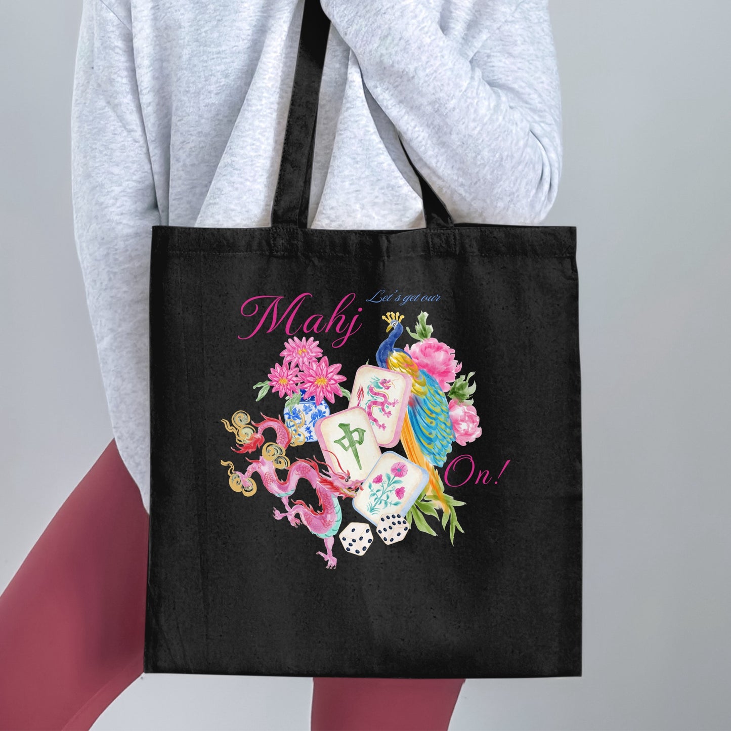 Black tote bag with pink text "Mahj Let's get our On!" and watercolor dragon, peacock, and mahjong tiles.