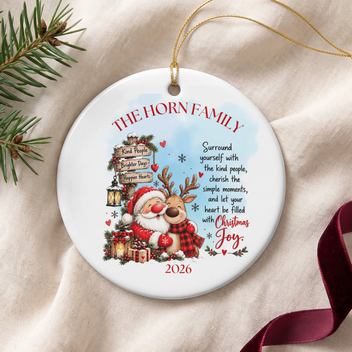 A round ceramic Christmas ornament featuring Santa and a reindeer hugging with customizable text and year 2026.
