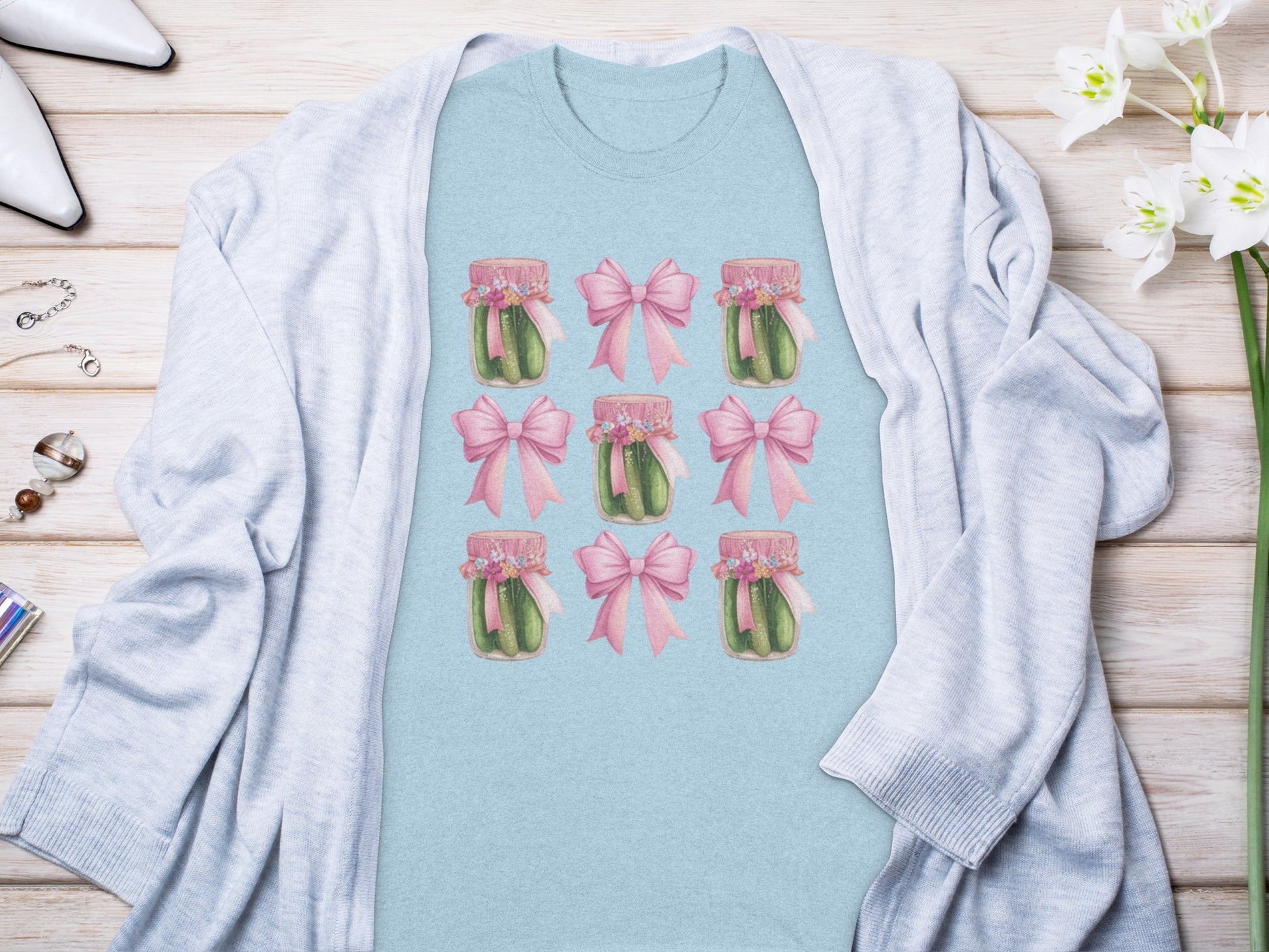 Light blue t-shirt with a repeated pattern of pickles in jars tied with pink bows.