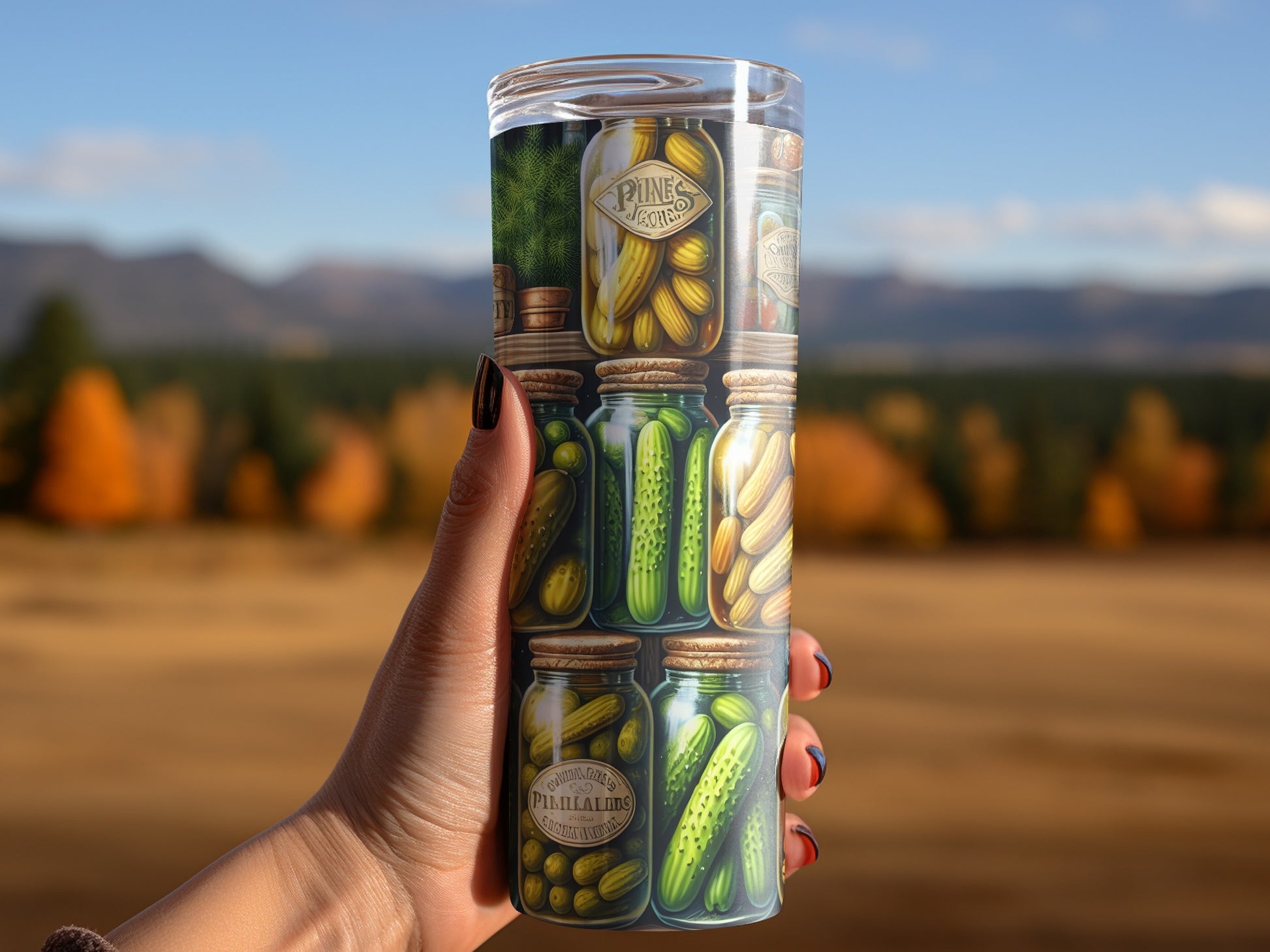 Hand holding tumbler with jars of pickles and autumn landscape background.