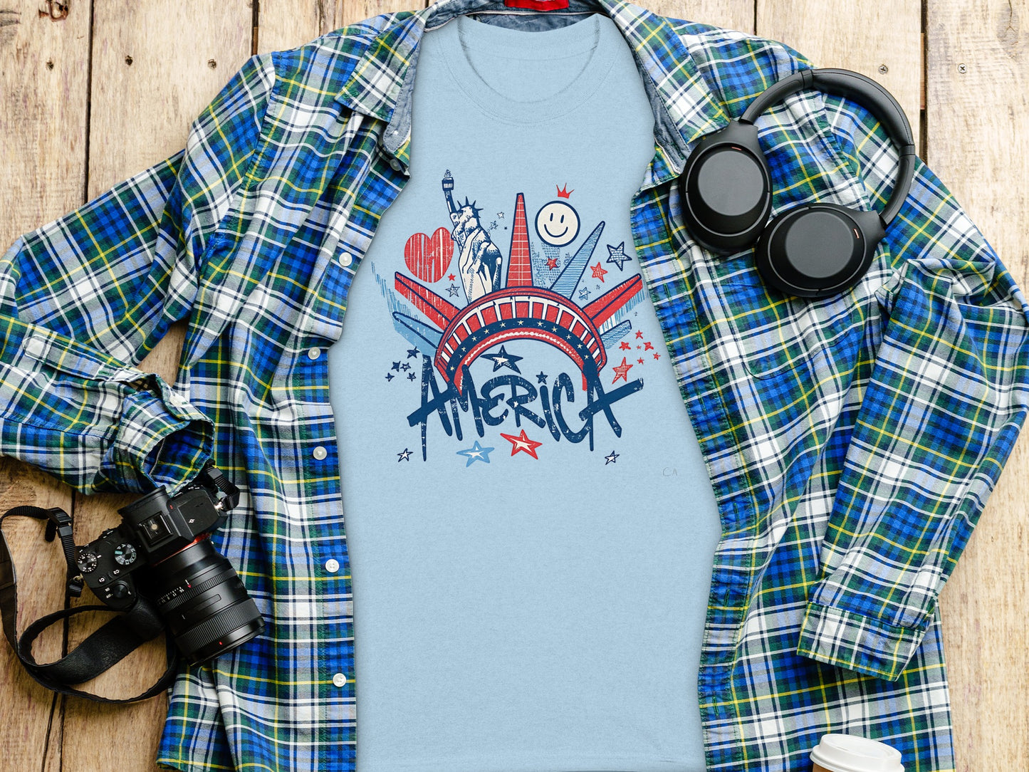 Light blue t-shirt with "America" text and patriotic icons, spread on a wooden surface.