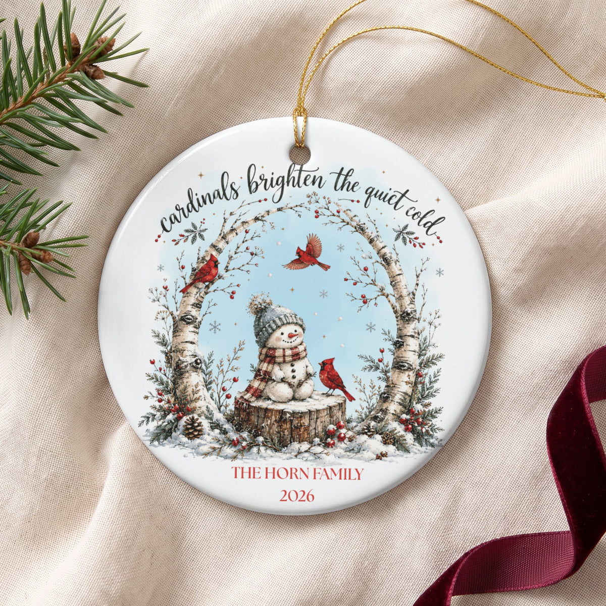 Round ceramic Christmas ornament with a snowman, red cardinals, birch trees, and personalized text.