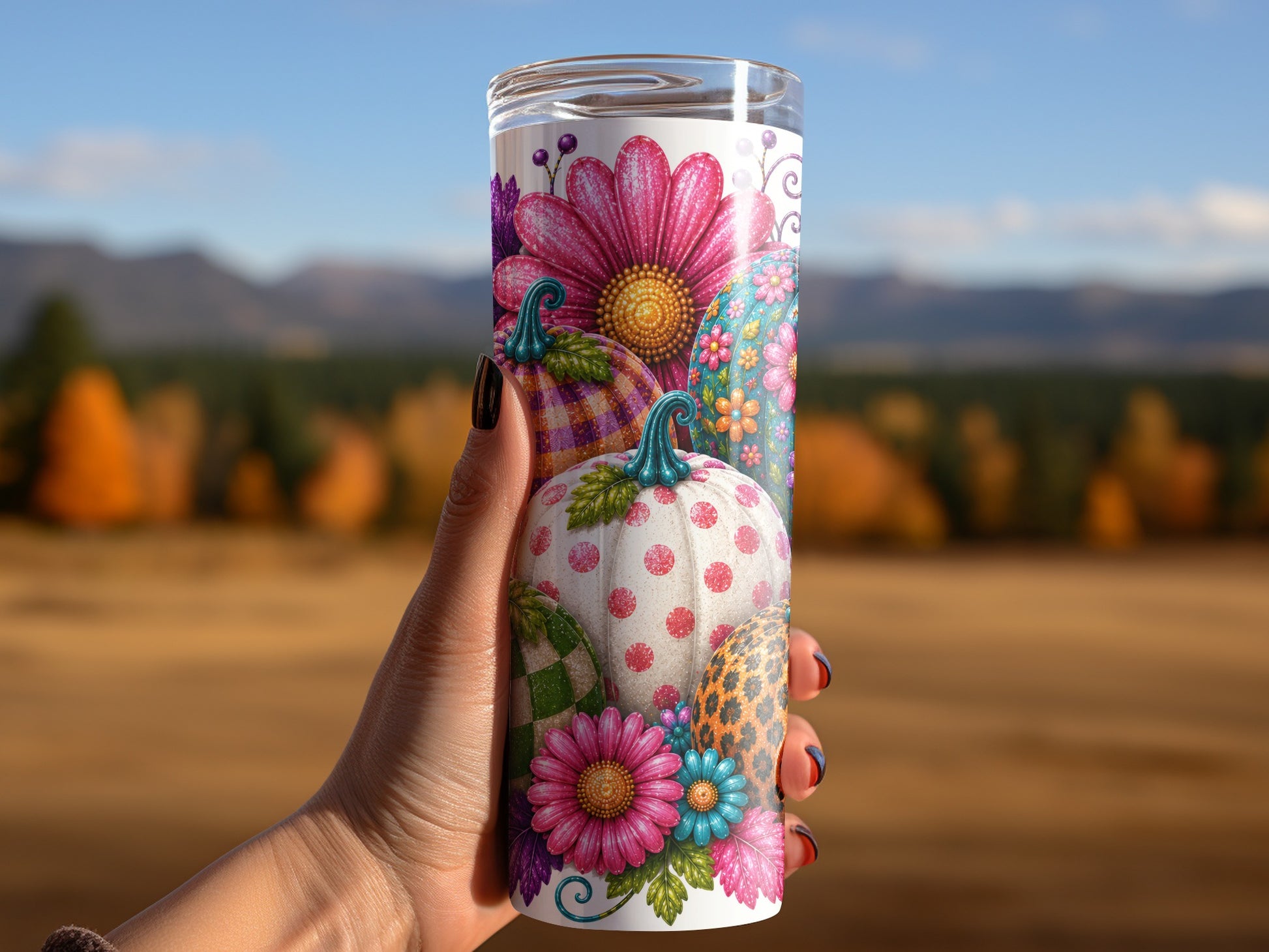 Tumbling tumbler with colorful, patterned pumpkins and flowers against a blurred outdoor landscape.