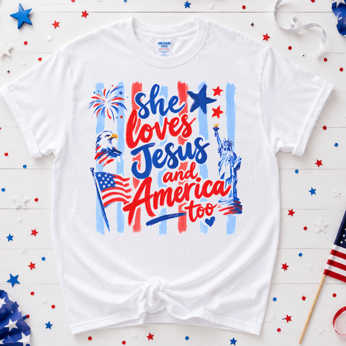 White t-shirt with patriotic design featuring text and symbols on a wooden background with American flags and stars.
