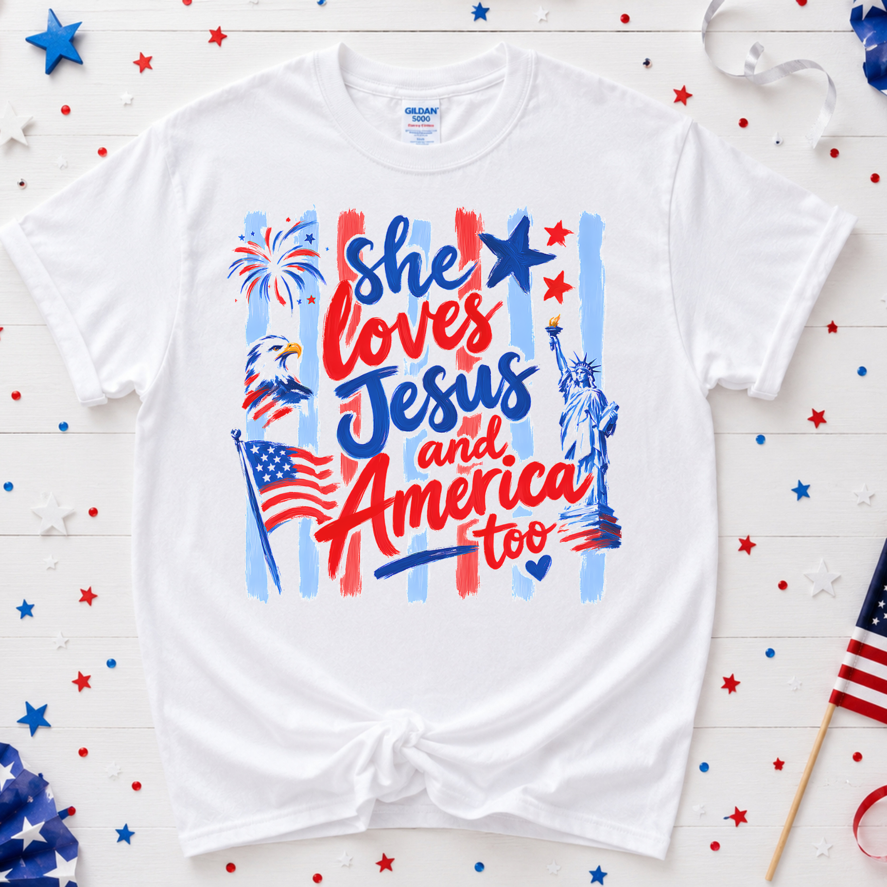 White t-shirt with patriotic design featuring text and symbols on a wooden background with American flags and stars.