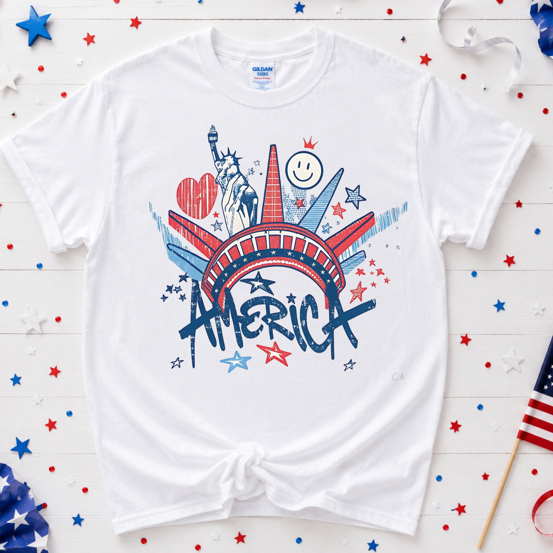 White t-shirt with 'AMERICA' graphic design on a wooden surface with decorative items.