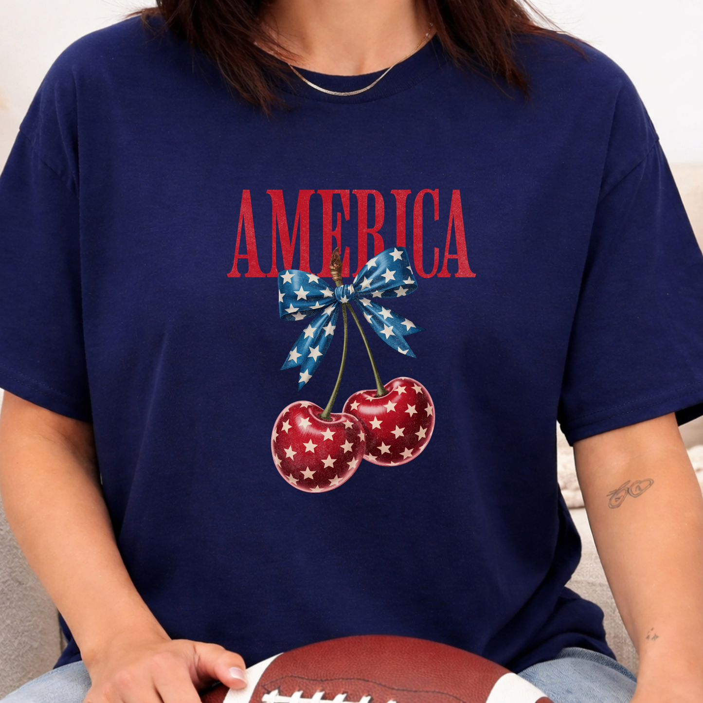 Navy blue t-shirt with 'AMERICA' and cherry design, held by a person.