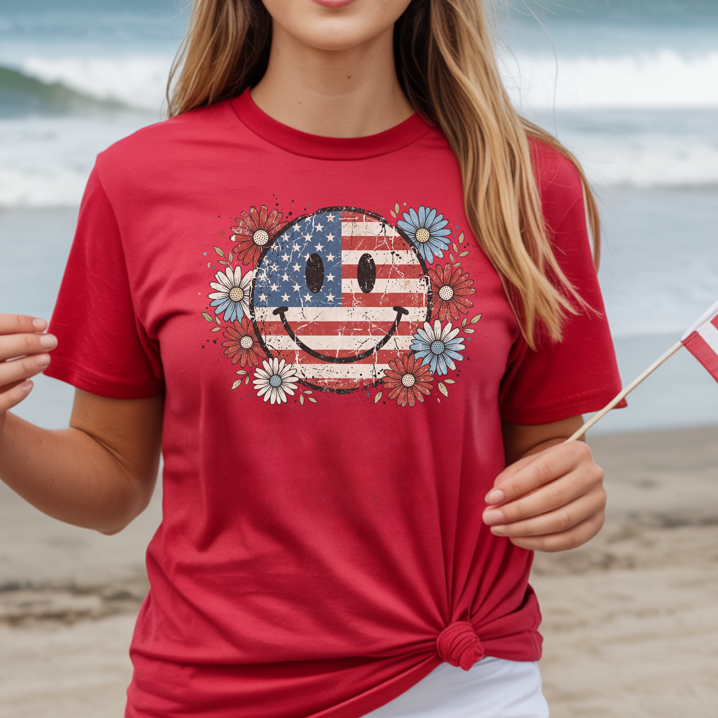 Person wearing a red t-shirt with a smiley face design featuring an American flag on a beach.
