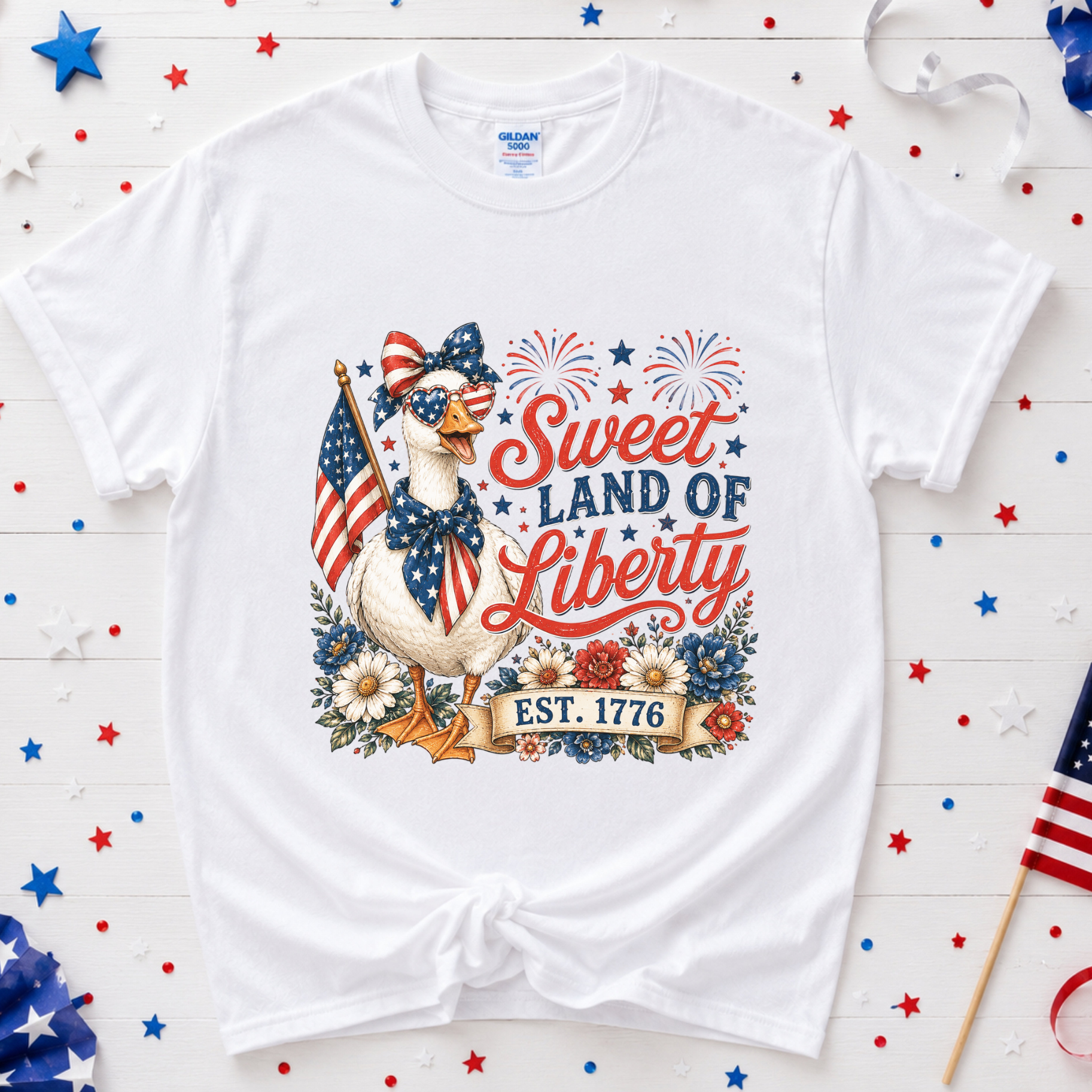 White t-shirt with a patriotic design featuring a goose, stars, and stripes on a wooden background.