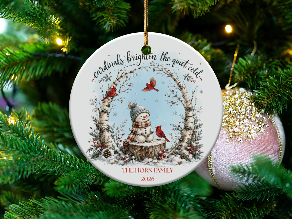 A round ceramic Christmas ornament featuring a snowman, red cardinals, birch trees, and personalized text.