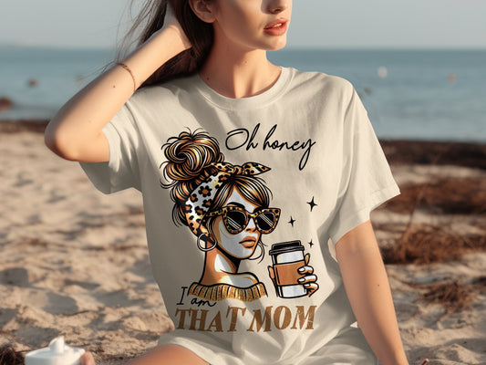 Woman wearing "Oh honey I am THAT MOM" shirt holding coffee cup on beach.