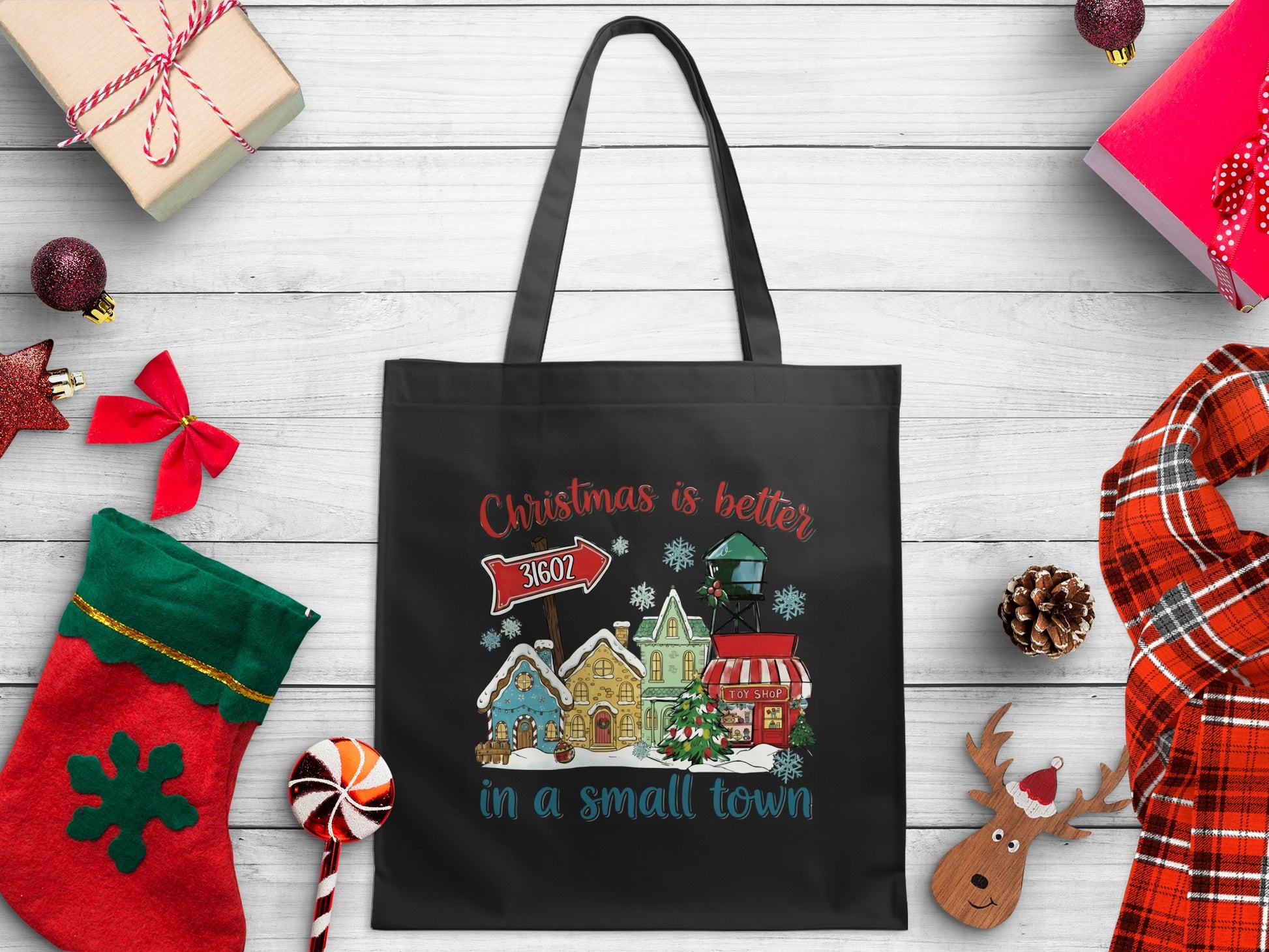 Black tote bag with "Christmas is better in a small town" text and village scene.