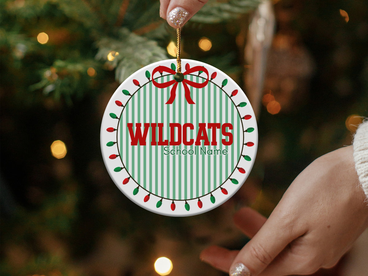 Round ornament with "WILDCATS" and "School Name" on green stripes, framed by lights.