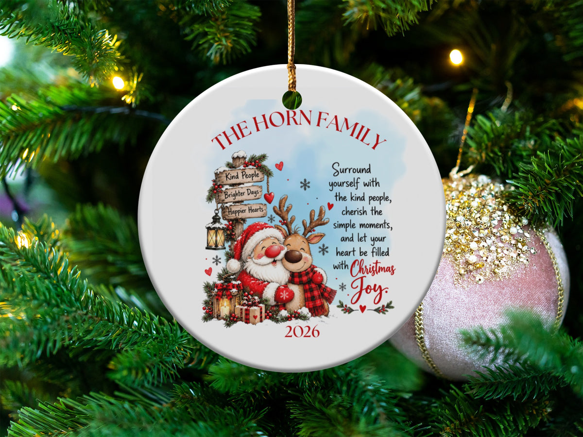 Round white ceramic Christmas ornament featuring a personalized family name, cartoon Santa, reindeer, and inspirational holiday text.