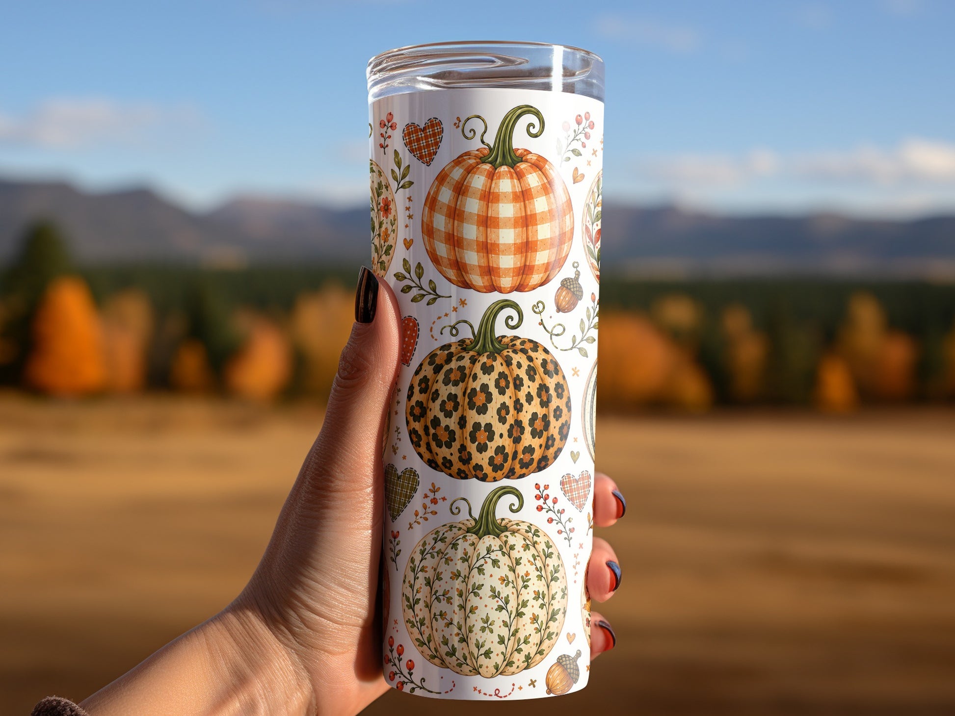 Tumbler with three decorated pumpkins and autumn motifs held outdoors.