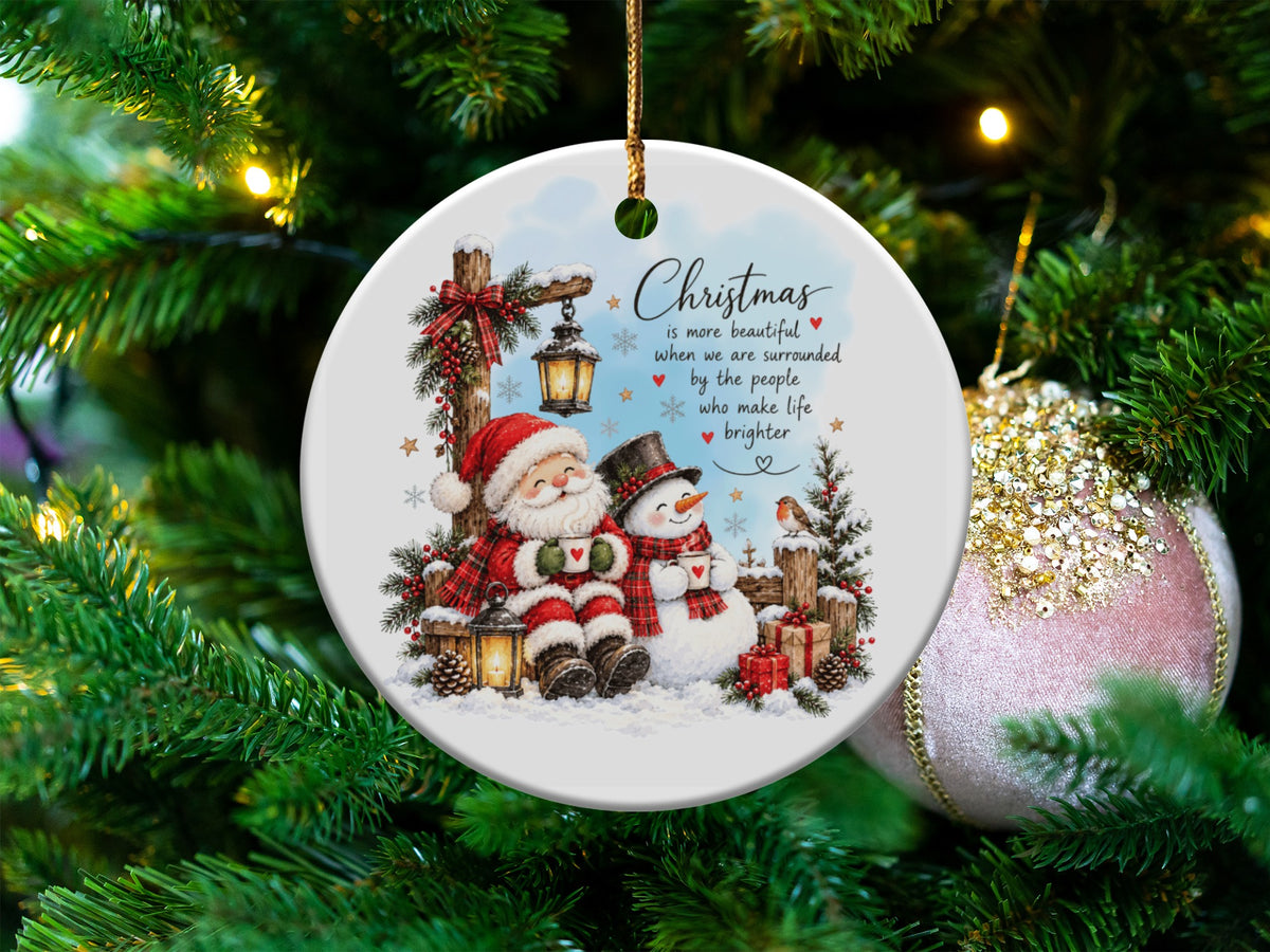 Round white ceramic Christmas ornament featuring Santa and a snowman holding mugs, hanging on a tree.