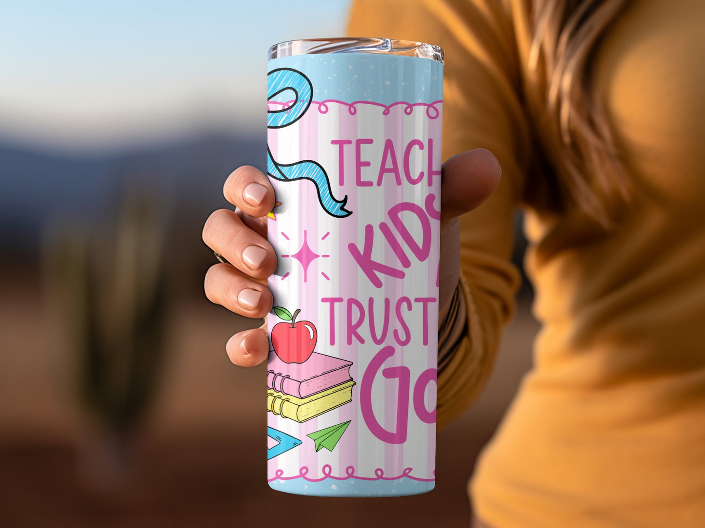 Tumbler with "Teach Kids Trust God" message, apple, books, and school supplies design.