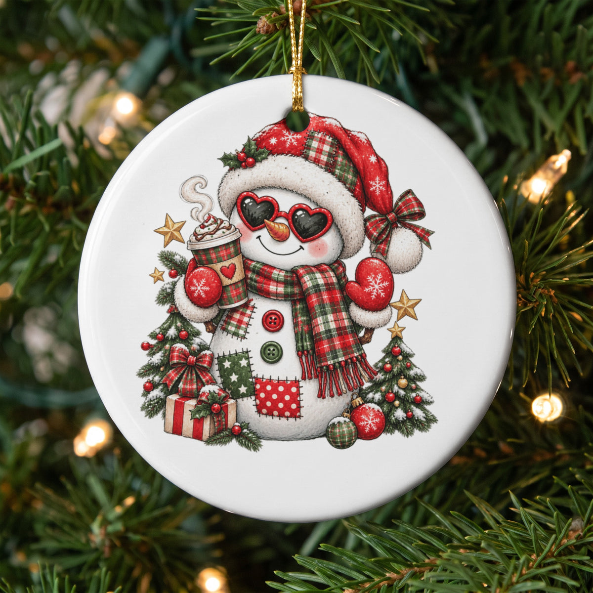 Christmas ornament with a snowman wearing heart sunglasses, holding hot chocolate, surrounded by trees and gifts.
