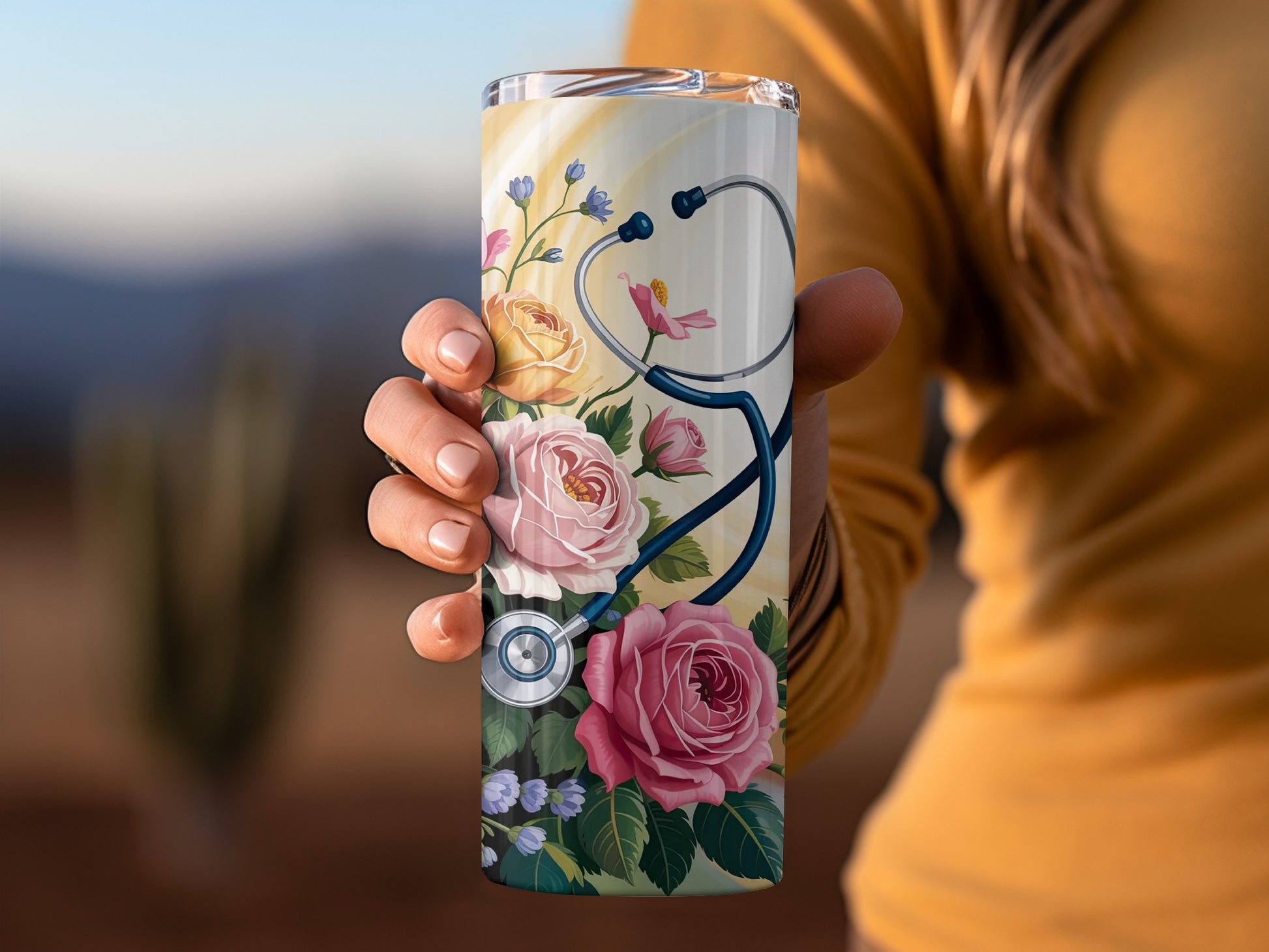 Tumbler with stethoscope and pink roses, held by a person.