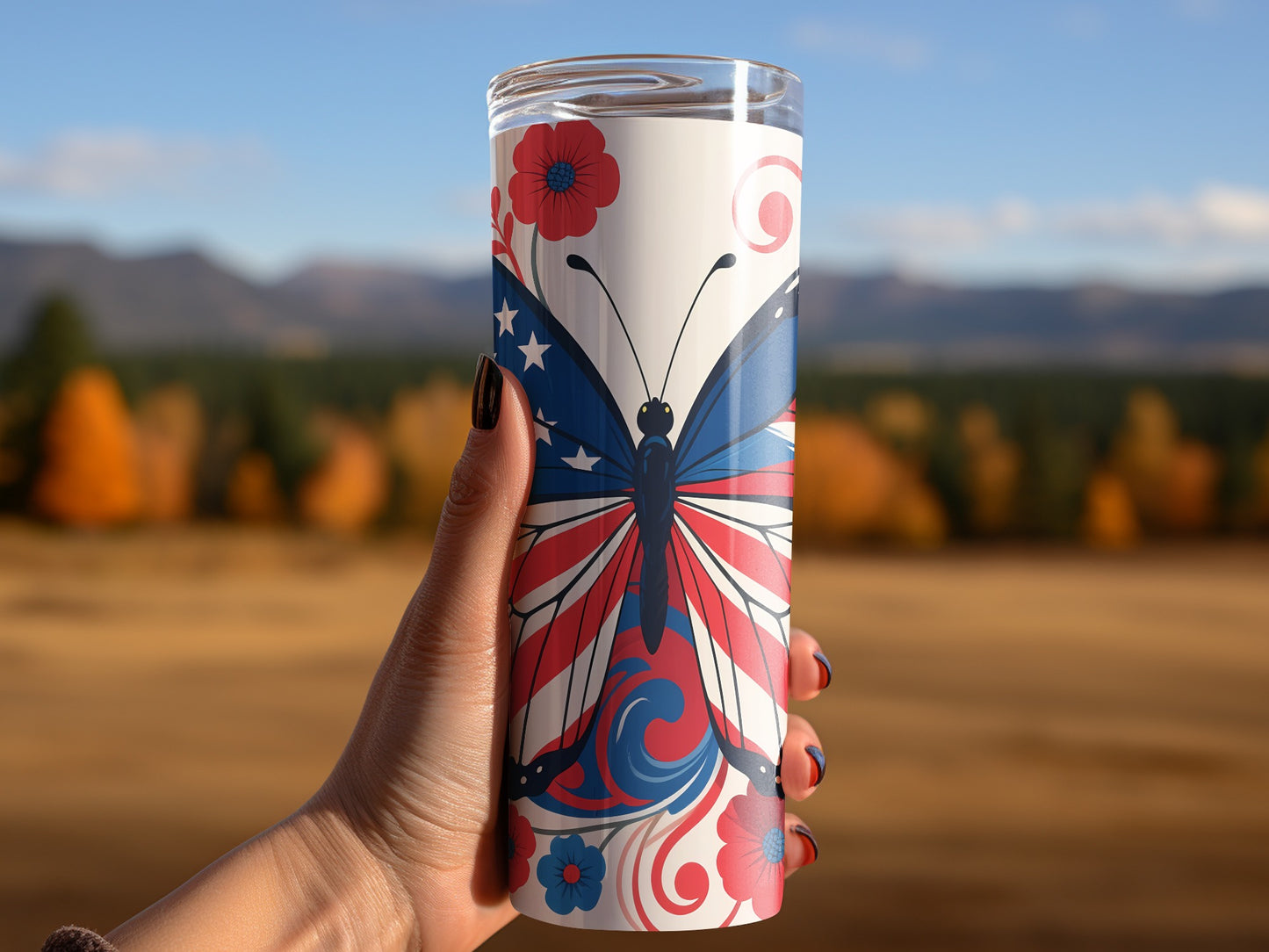 Tumbler with patriotic butterfly design held against blurred autumn landscape.