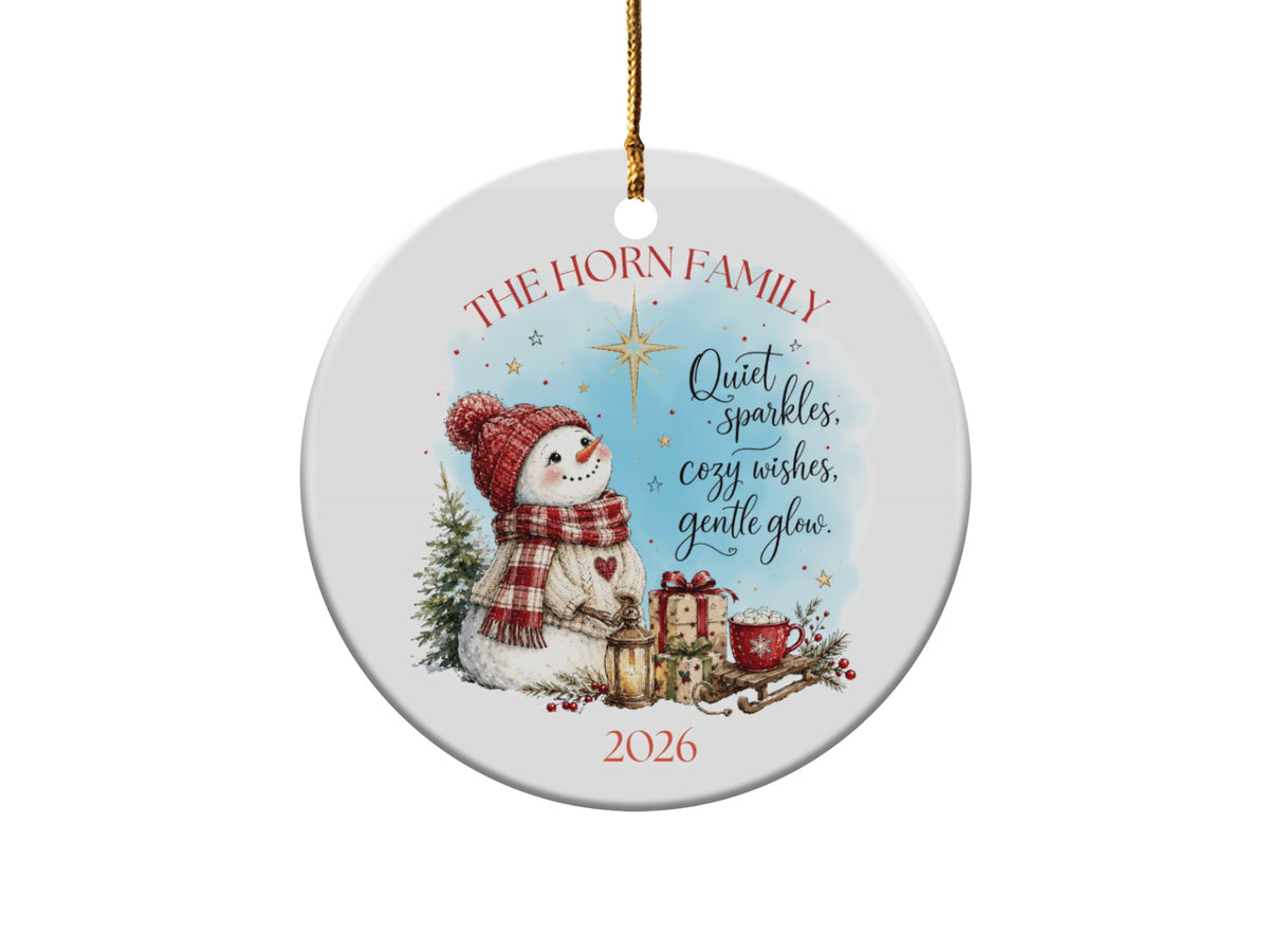 Round ceramic Christmas ornament featuring a snowman, wrapped gifts, holiday text, and the year 2026.