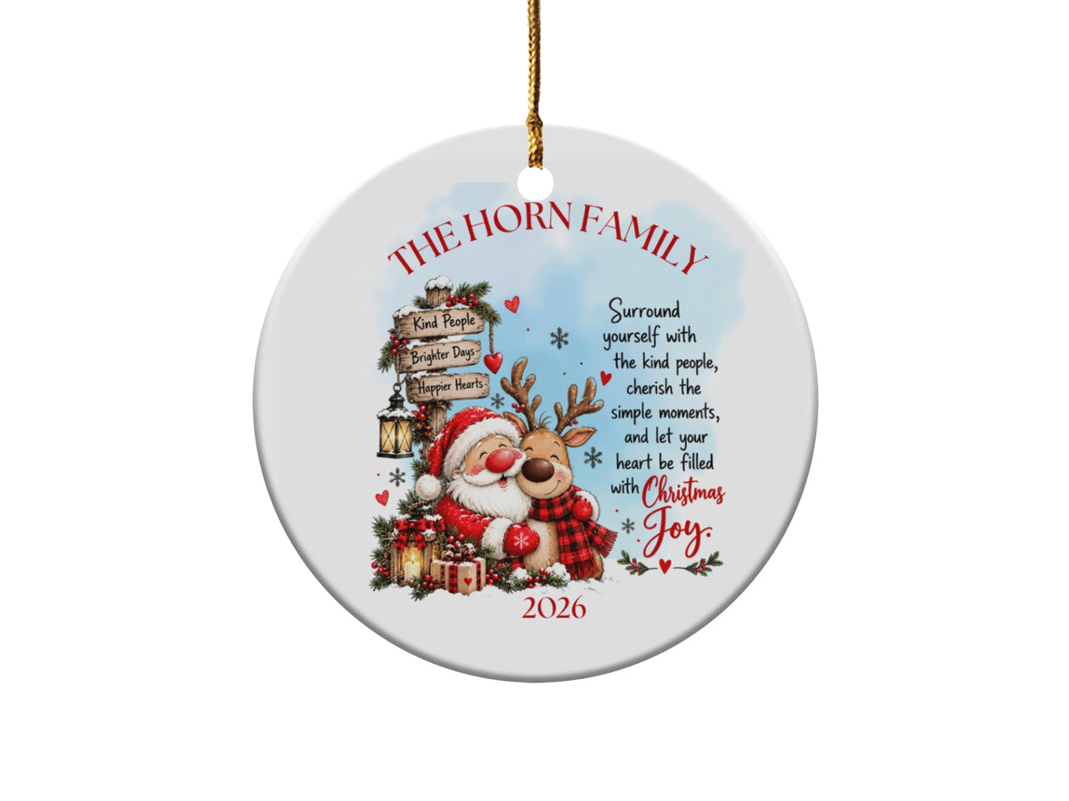 A round white Christmas ornament features Santa hugging a reindeer, family text, and the year 2026.