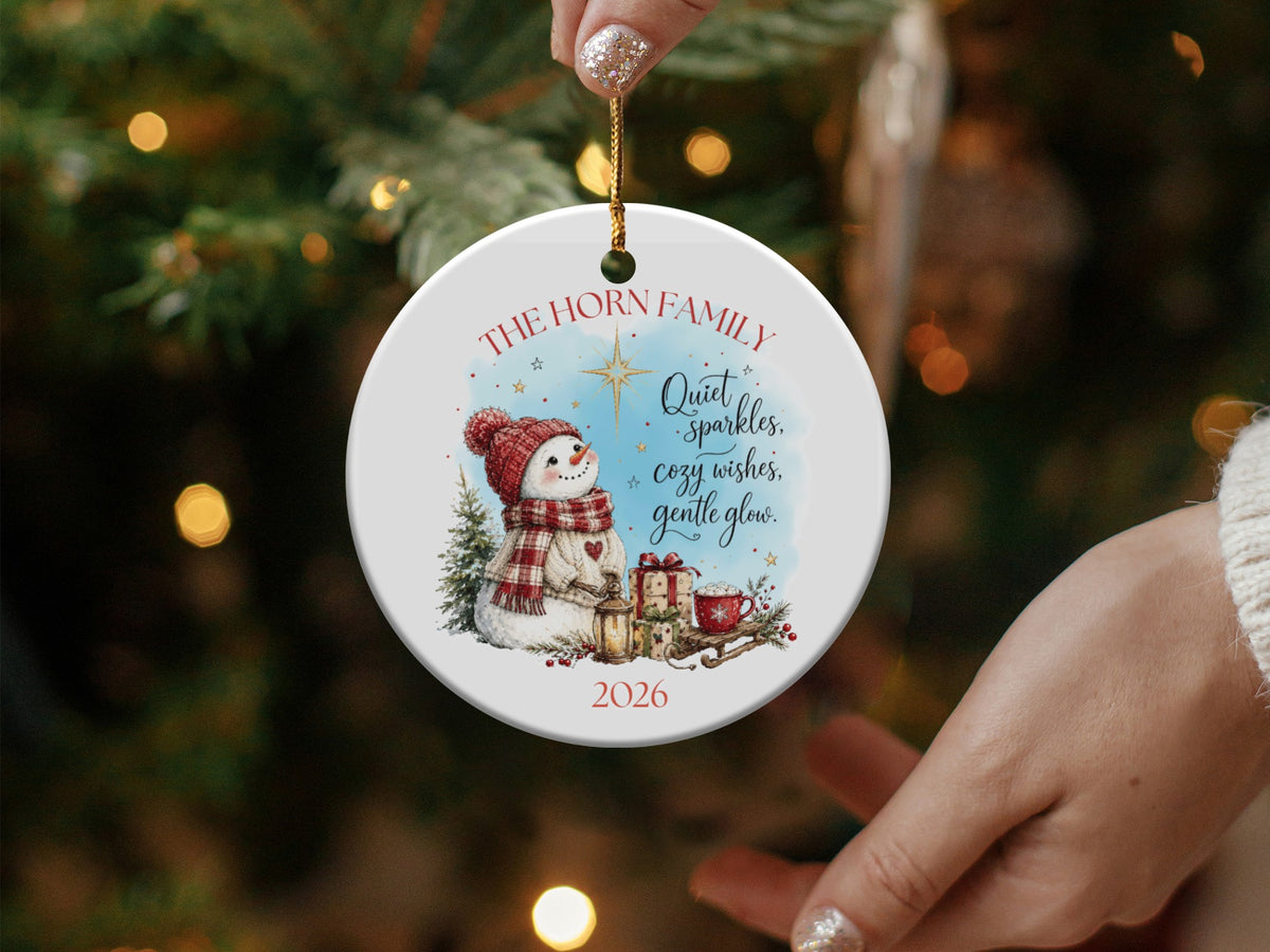 Round ceramic Christmas ornament with a watercolor snowman illustration, custom family name, year, and holiday text.