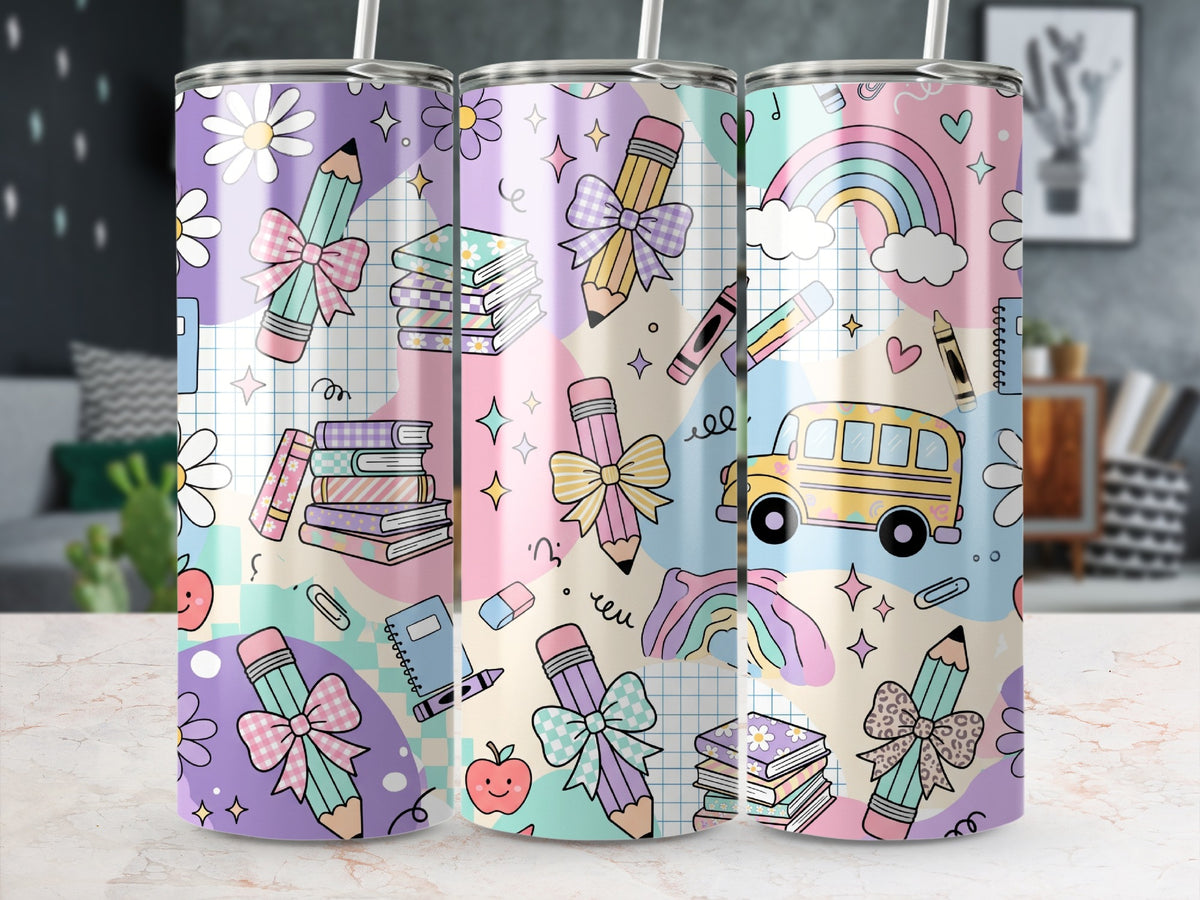 Three stainless steel travel tumblers stand on a marble surface, featuring a colorful school-themed pattern with pencils, books, and rainbows.