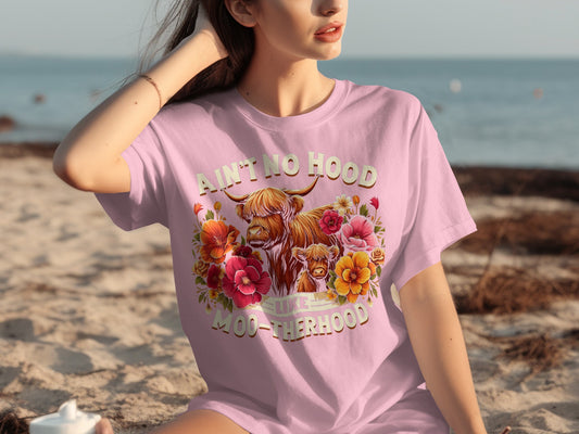 Pink t-shirt with Highland cows and floral graphic, "Ain't no hood like motherhood" text.