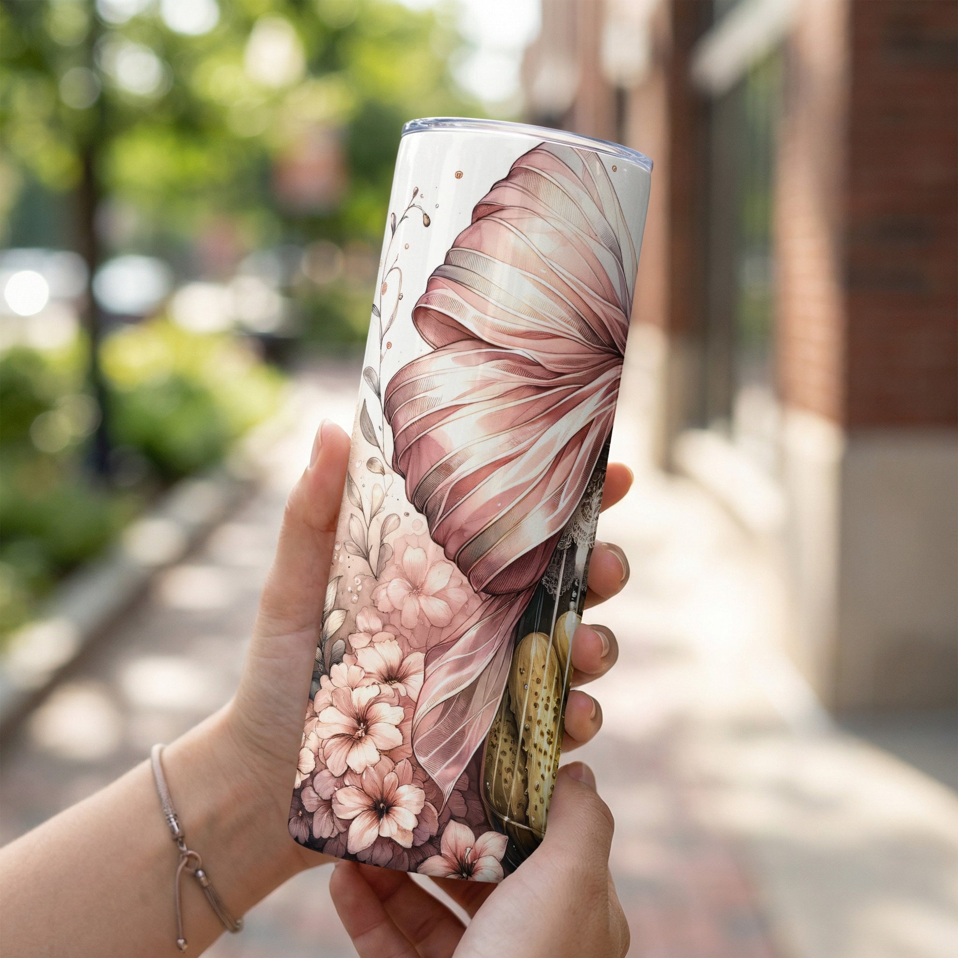 Tumbler with floral and bow pattern held by hands outdoors.
