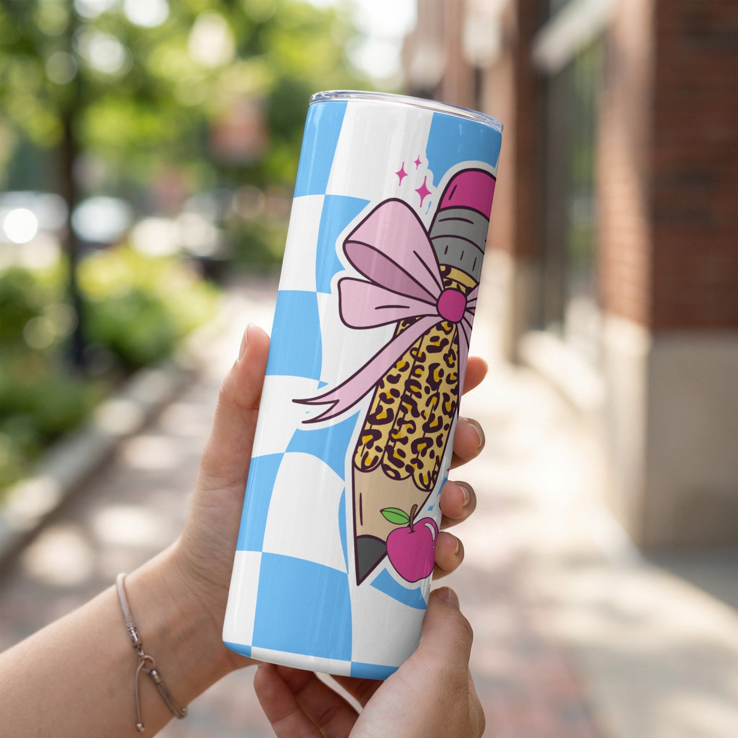Tumbler with pencil, bow, leopard print, and apple design on checkered background.