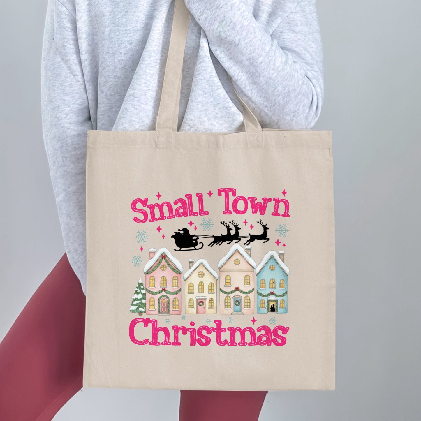 Canvas tote bag with pink text "Small Town Christmas" and festive Christmas village illustration.