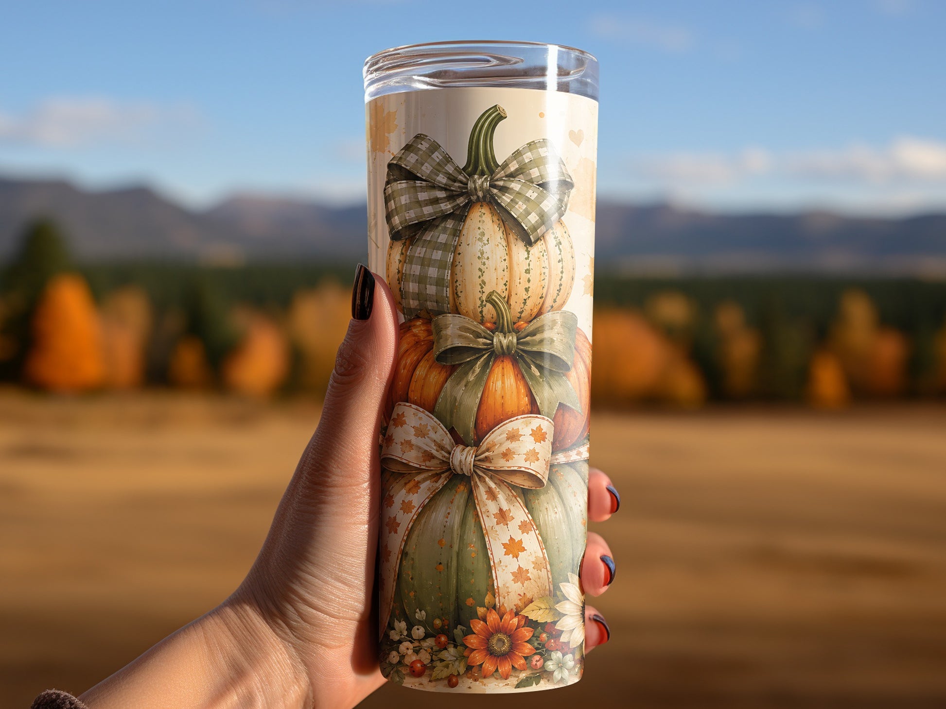 Tumbler with stacked pumpkins, bows, and autumn leaves pattern held by a hand.