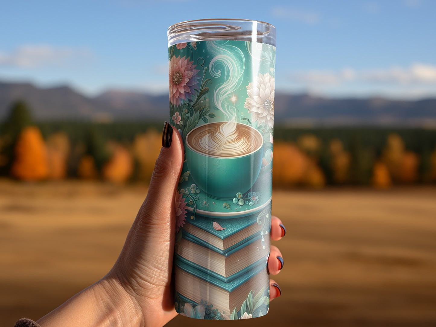Blue floral tumbler with coffee cup design on blurred landscape background.
