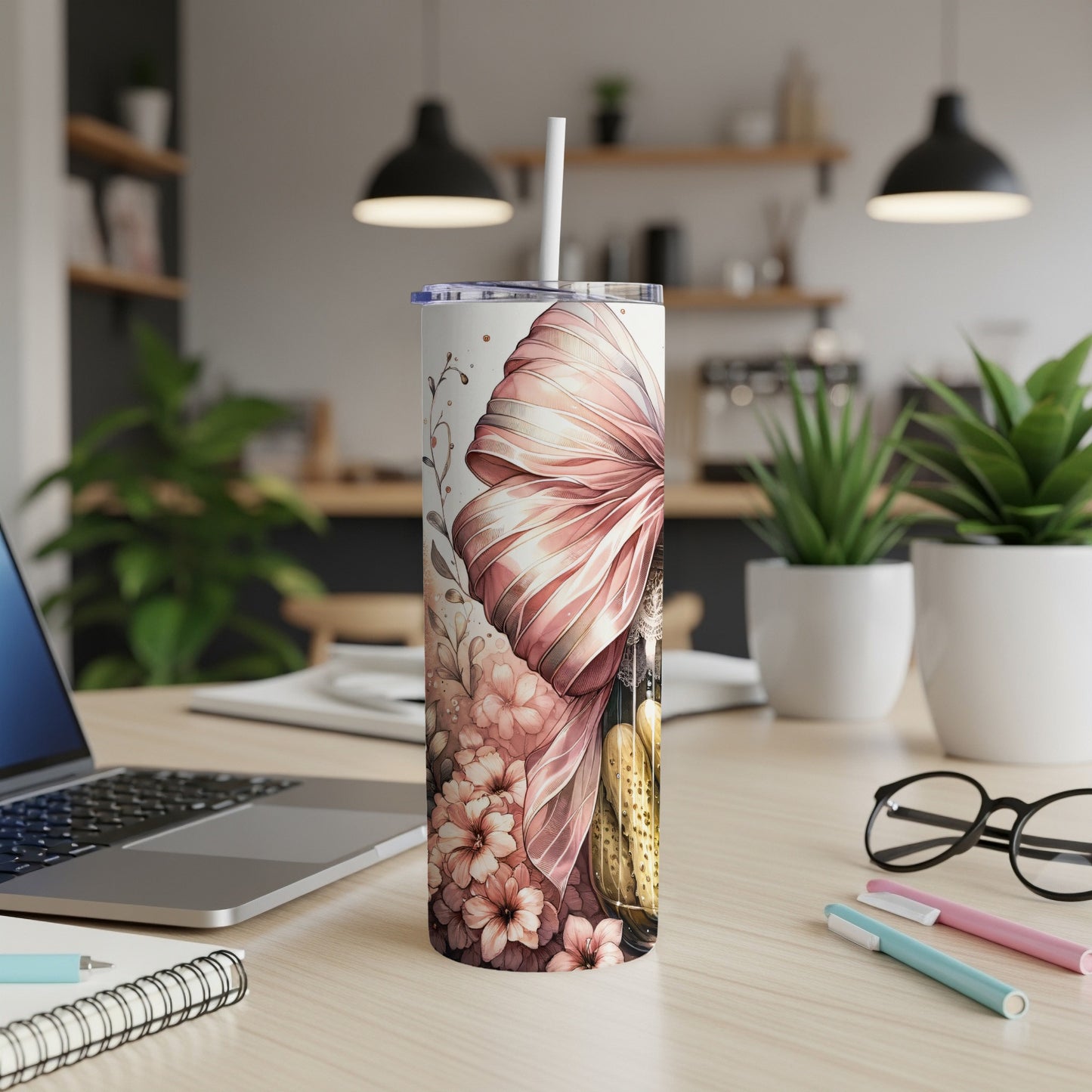 Floral tumbler with pink bow on desk next to laptop and pens.