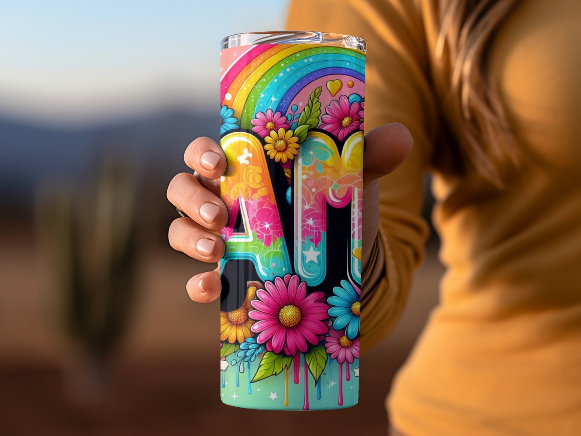Rainbow and flowers design on a tumbler held by a hand.