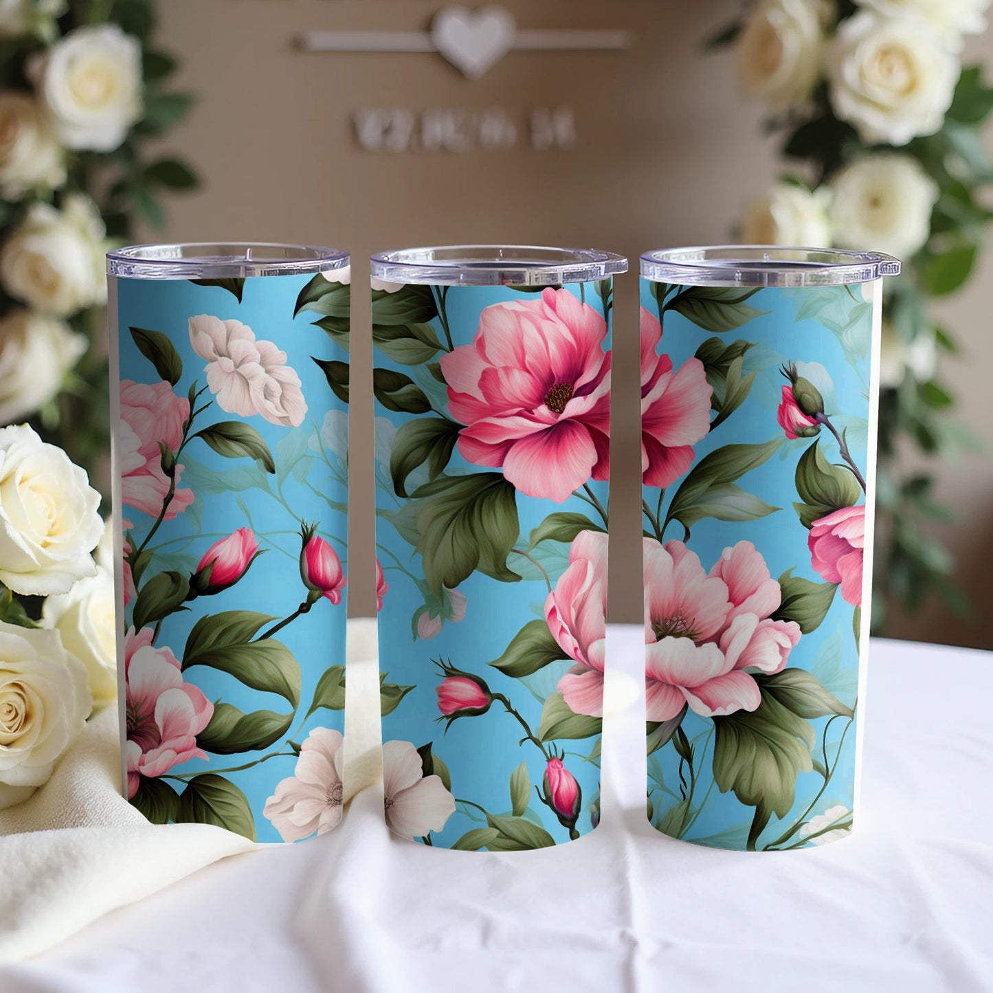 Three blue tumblers with pink floral patterns on a white tablecloth.