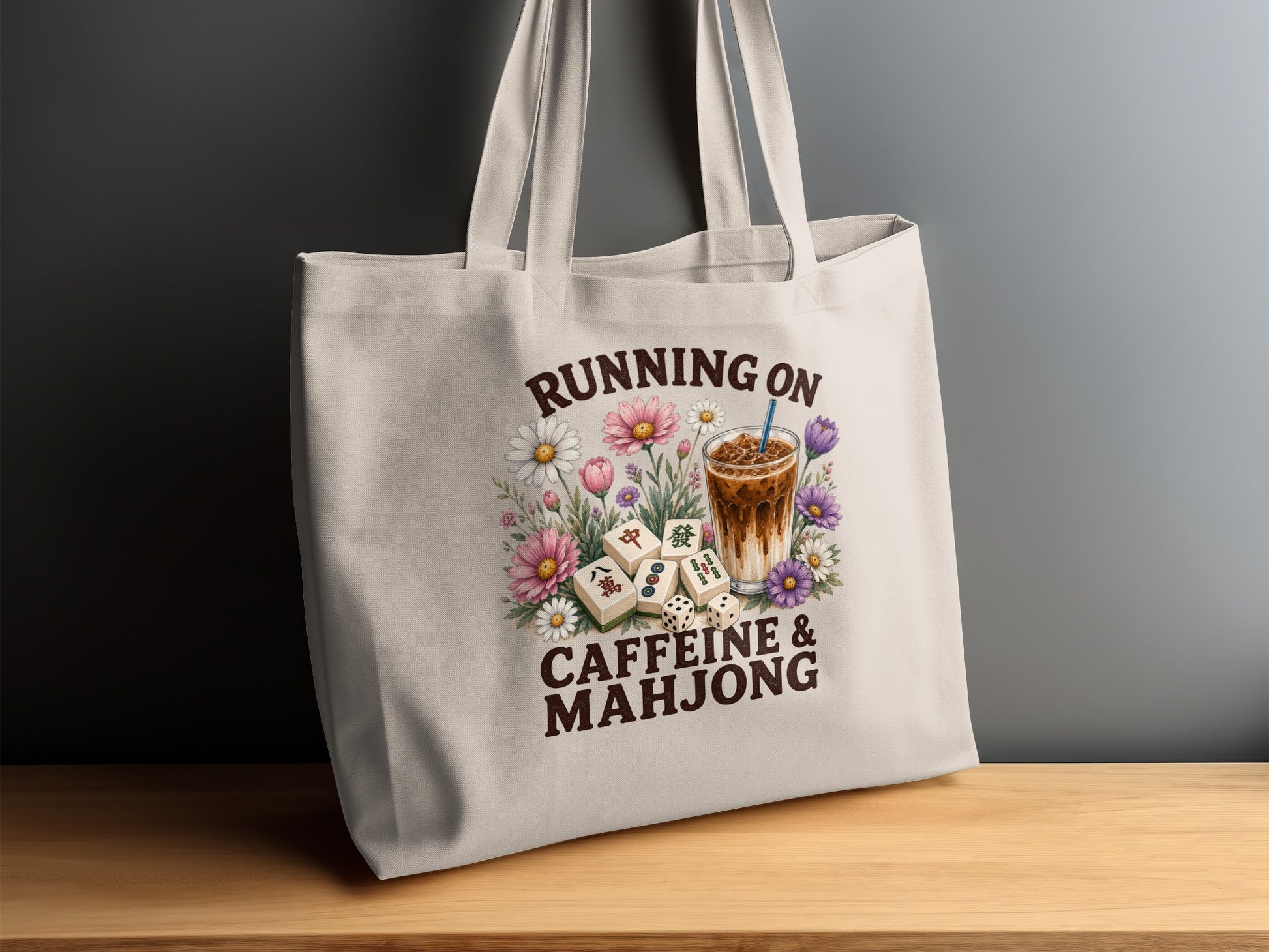 Tote bag with "Running on Caffeine & Mahjong" text, iced coffee, dice, and flowers.