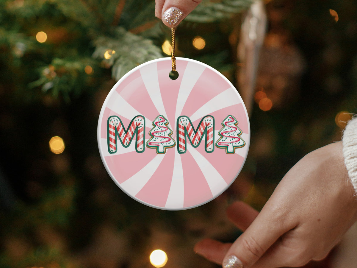 Round ceramic ornament with "MAMA" spelled out in gingerbread cookie letters against a pink sunburst background.