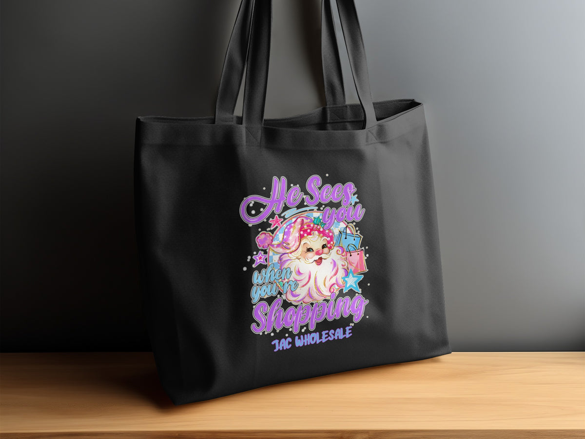 Black tote bag with Santa graphic saying "He Sees You When You're Shopping."