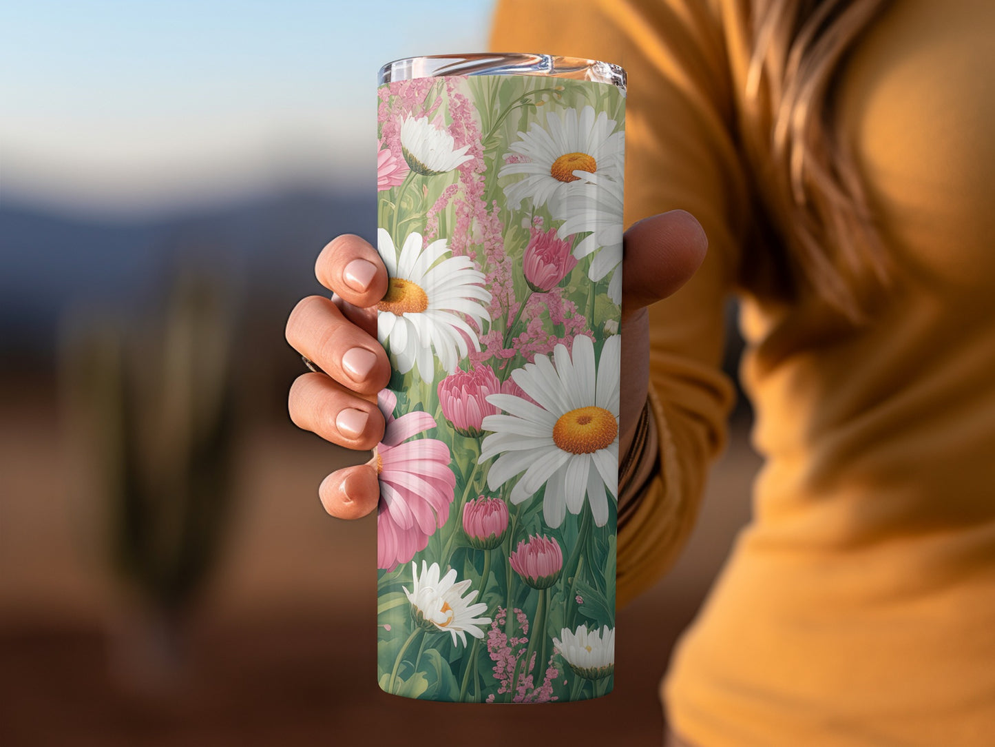 Tumbler with daisies and pink flowers, held by a person.