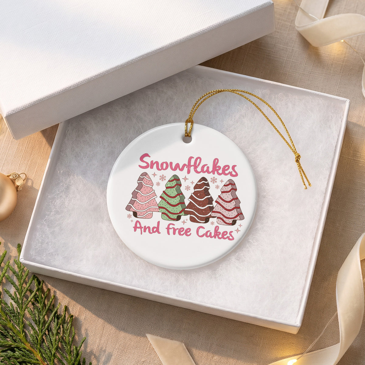 Round ceramic ornament with trees, "Snowflakes And free Cakes" text, in gift box.