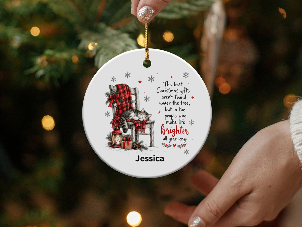 A round ceramic Christmas ornament featuring a sleeping cat on a chair, holiday text, and the name Jessica.