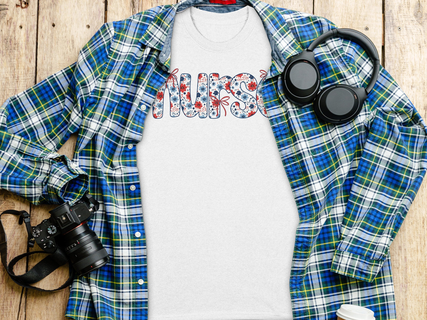 White t-shirt with "NURSE" in floral letters, displayed with plaid shirt and headphones.